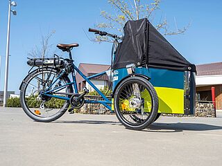 Présentation d'un vélo cargo électrique aux couleur bleu et jaune avec logo Vélila. Capote antipluie fermée. - Agrandir l'image, .JPG 273 Ko (fenêtre modale)