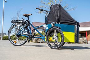 Présentation d'un vélo cargo électrique aux couleur bleu et jaune avec logo Vélila. Capote antipluie fermée.